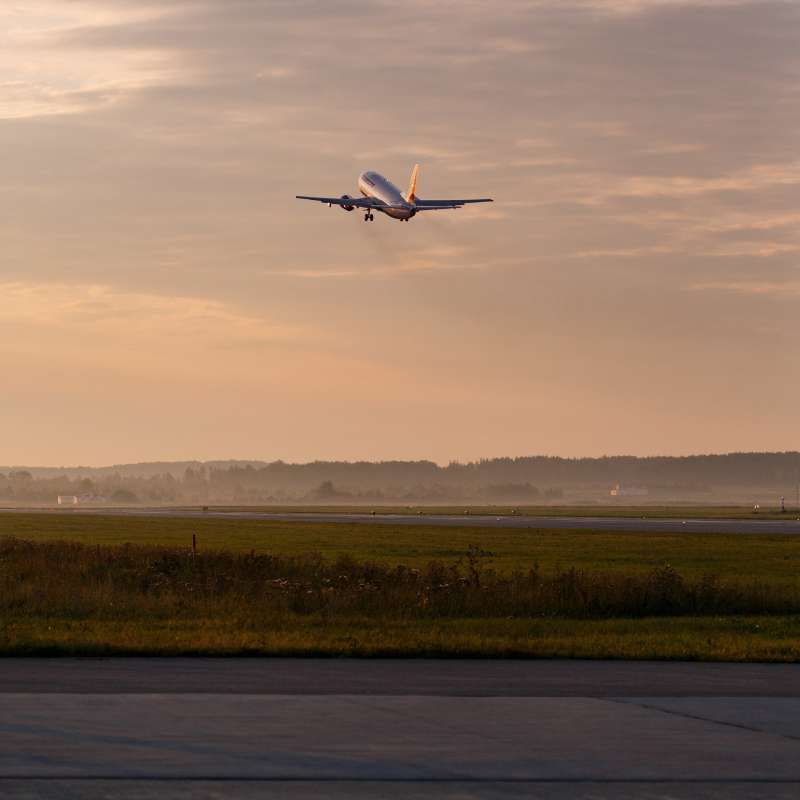Ein Passagierflugzeug hebt bei Sonnenuntergang vom Rollfeld ab. Ohrendruck beim Fliegen entsteht oft beim Start und der richtige Gehörschutz kann dabei vorbeugen.