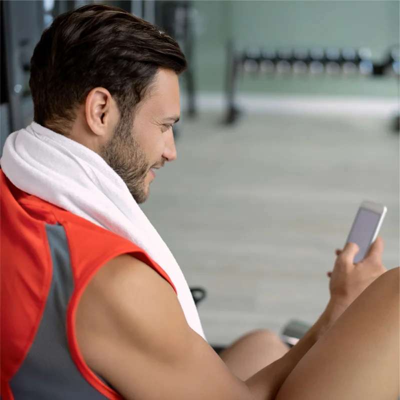 Mann mit Smartphone im Fitnessstudio – Starkey Edge AI lässt sich bequem per App steuern.