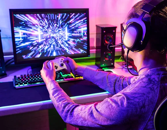 Junger Gamer mit Kopfhörern spielt intensiv ein Videospiel, hervorhebend das Risiko von Hörverlust durch laute Spielgeräusche und die Wichtigkeit von Gehörschutz.