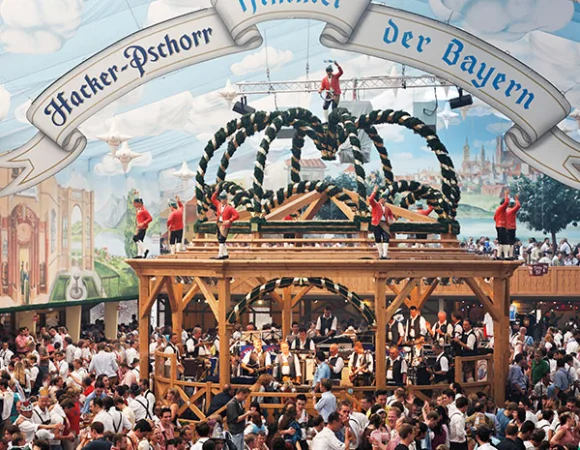 Menschenmenge feiert auf dem Oktoberfest, viele tragen Gehörschutz, um trotz des Lärms ihre Ohren zu schützen.