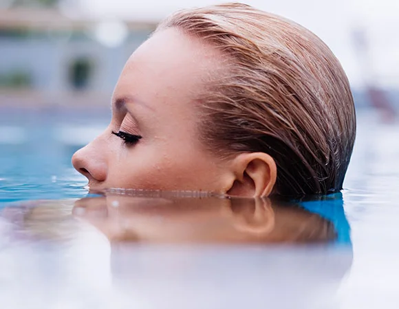 Nahaufnahme einer Frau mit leicht über Wasser schwebendem Kopf, symbolisierend die Gefahr von Wasser im Ohr und die Notwendigkeit präventiver Maßnahmen.