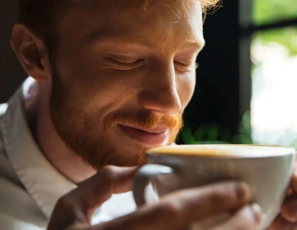 Mann schließt entspannt die Augen und kostet genüsslich seinen Kaffee. Der Moment steht sinnbildlich für moderater Kaffeegenuss und Gehörgesundheit.